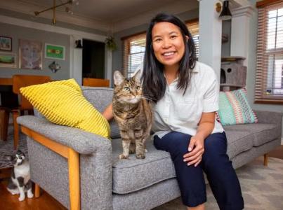 Smiling person sitting next to a cat on a couch