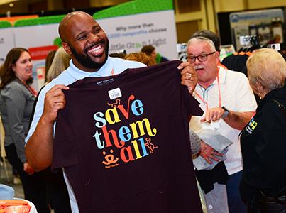 Smiling person holding a 'Save Them All' T-shirt at the Best Friends National Conference