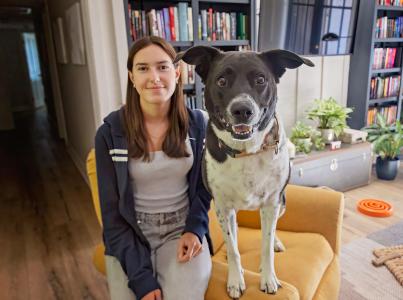 Woman and large brown and white dog sitting on edge of yellow chair in living room setting 