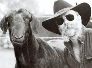 Man in cowboy hat wearing sunglasses standing next to goat