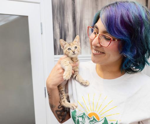 Smiling person with multi-colored hair holding a kitten
