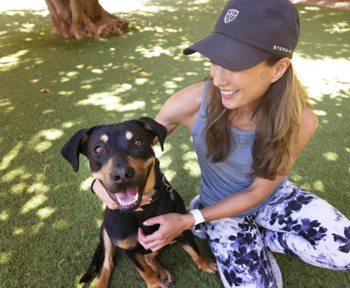 Smiling dog outside on some grass being held by a person wearing a hat