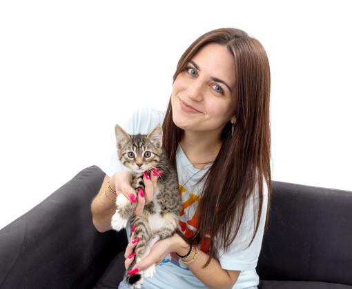 Smiling person sitting on a couch holding a tabby kitten