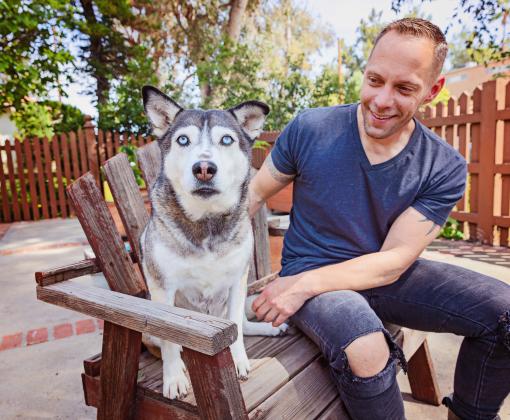 Smiling person sitting with a big dog in a chair on a patio