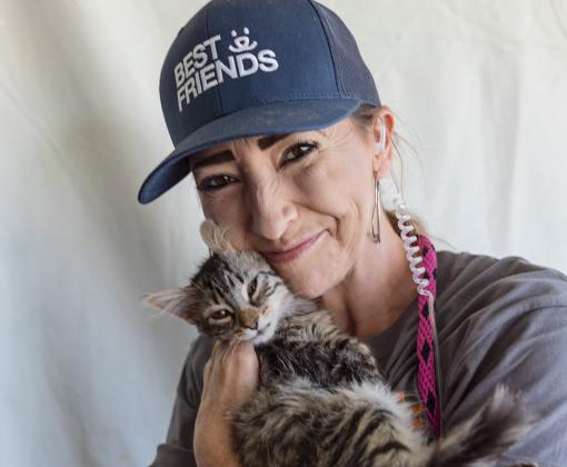 Smiling person wearing a hat cradling a tabby cat