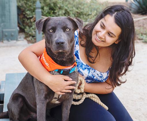Smiling person outside with a leashed dog wearing a bandanna