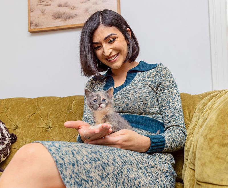 Person on a couch smiling and holding a foster kitten