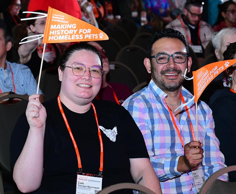 People in the audience at a Best Friends National Conference holding orange flags that say, 'Making history for homeless pets'