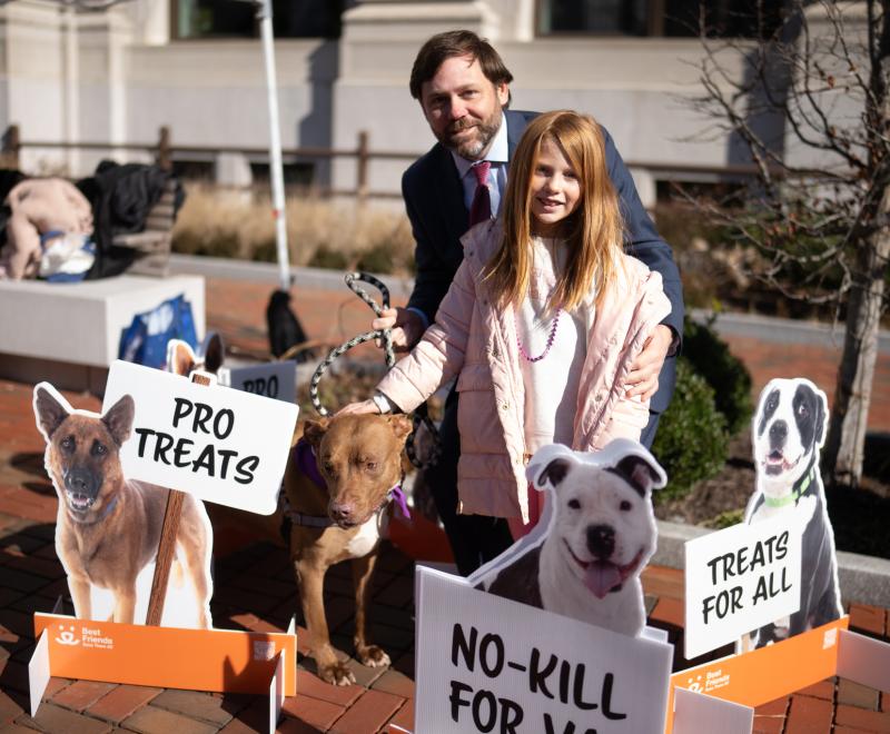 A father and daughter and their dog holding up signs that say "pro treats" and "treats for all"