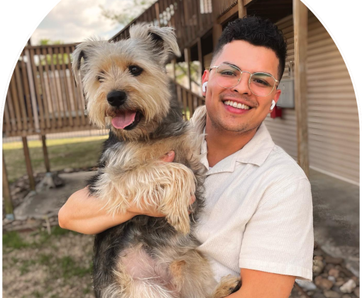 A smiling man hold up a furry black and gray dog