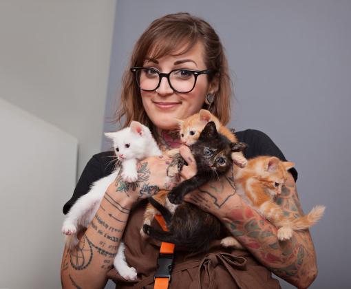 Smiling person holding a litter of kittens