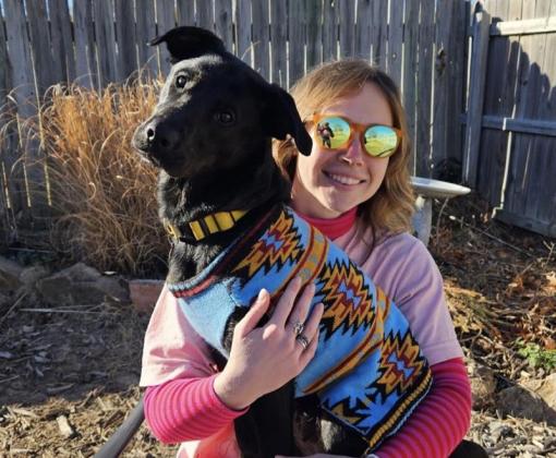 A woman holds a black dog wearing a sweater