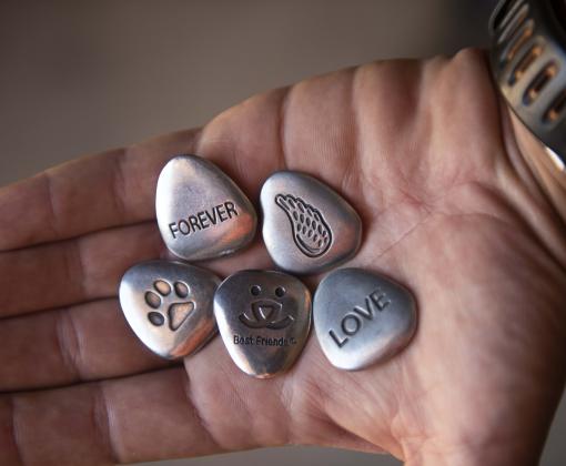 Person holding pet memorial tokens in the palm of their hand. Pet memorial tokens can be a comforting gift for someone grieving the loss of a pet.