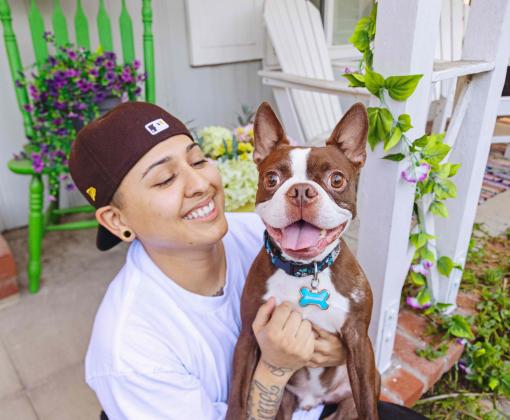 Smiling person holding a small, happy brown and white dog outside on a front porch