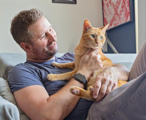 man lying on couch holding orange tabby cat