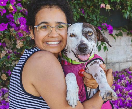woman holding medium white and brown dog close among flowers