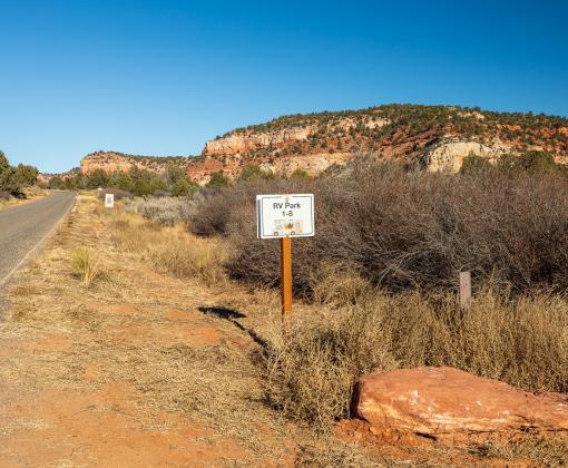RV Park 1-8 sign beside a road in front of a red rock cliff