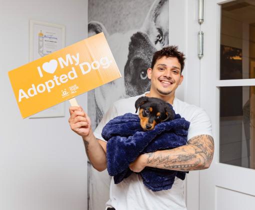 Smiling person holding a puppy and a sign that says "I heart my adopted dog"