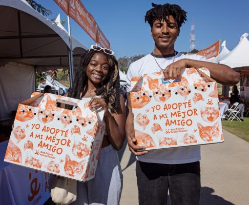 Two smiling people holding pet carriers at a pet adoption event