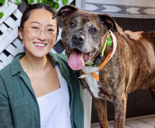 Smiling person sitting next to a dog on a step outside