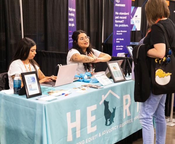 Exhibitors at a booth at the Best Friends National Conference talking to an attendee