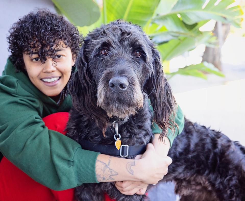 Smiling person hugging a curly haired, black dog