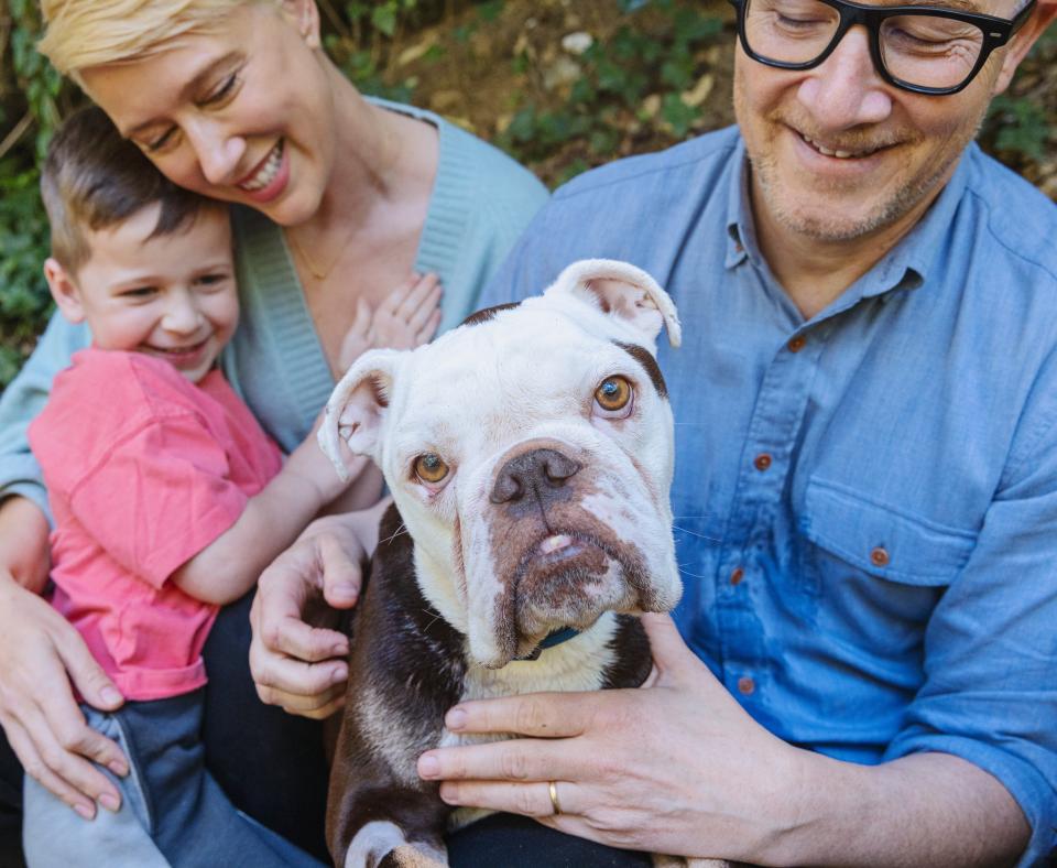 Bulldog surrounded by a loving family outside in front of some folliage
