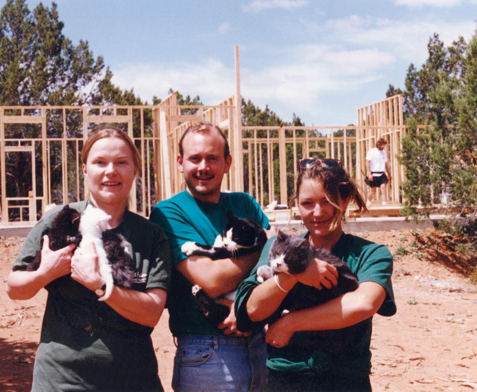 Vivian, Judah and another person holding cats in front of the construction of a building