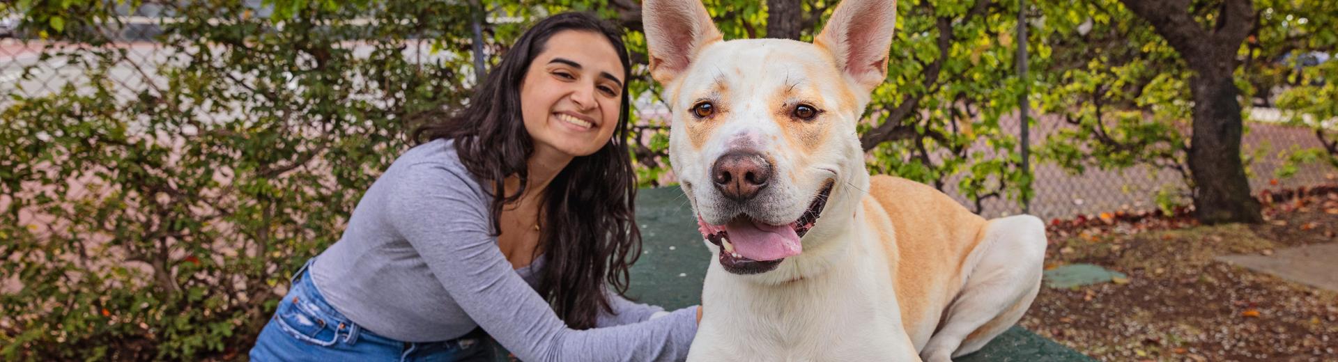 Smiling person sitting outside with a dog in a park