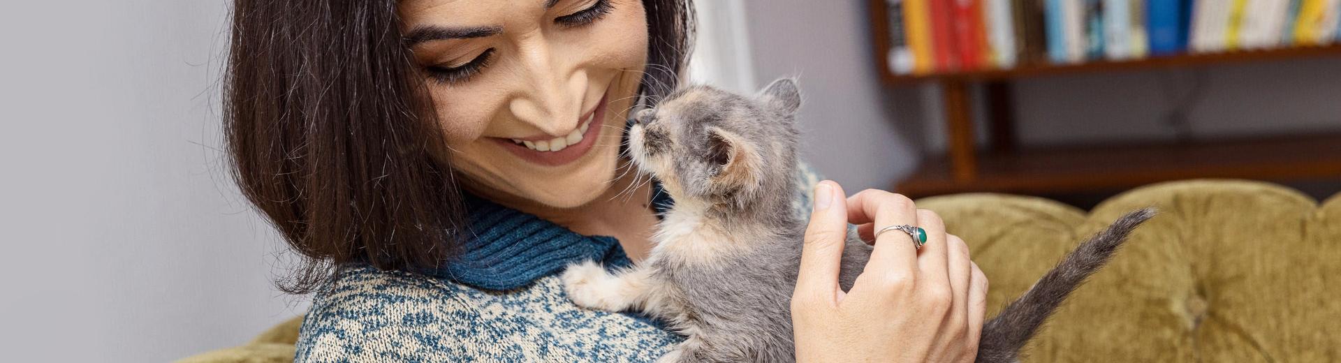 Smiling person holding a small dilute calico kitten