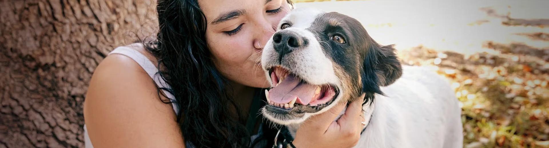 Smiling person hugging a dog in front of a tree