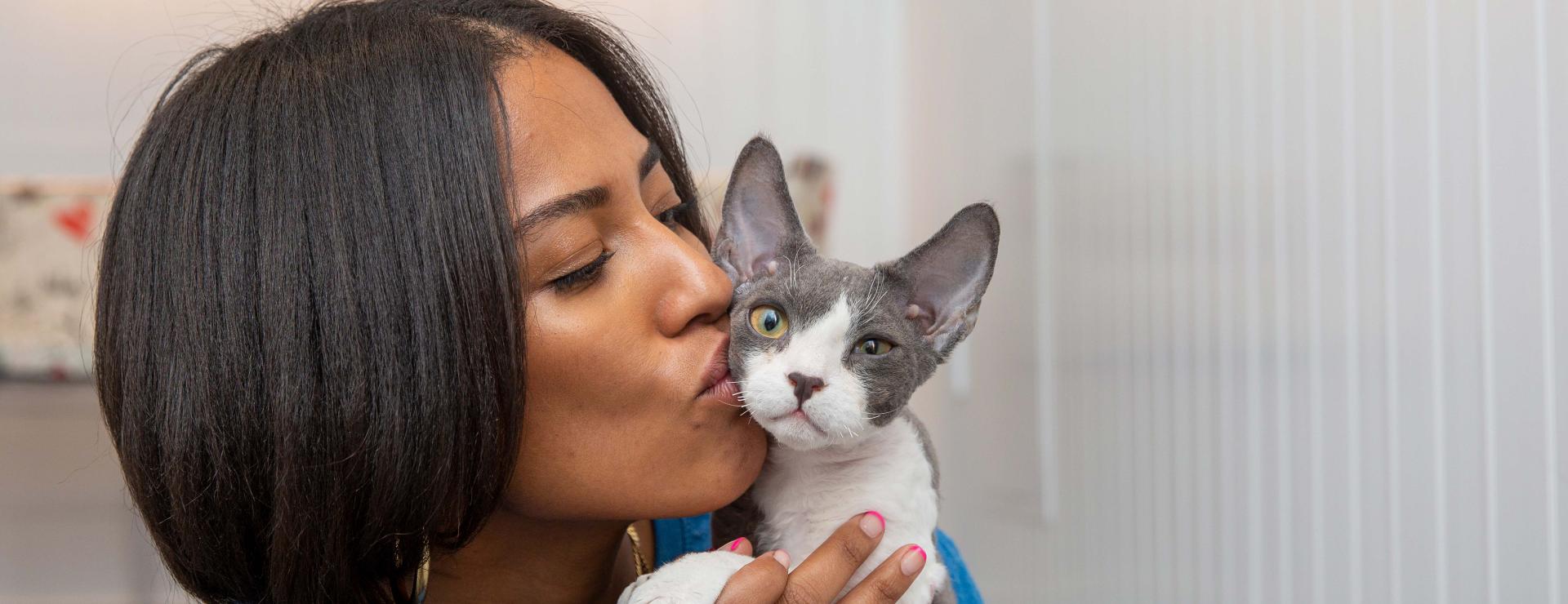 Smiling person kissing the side of the head of a hairless sphinx cat