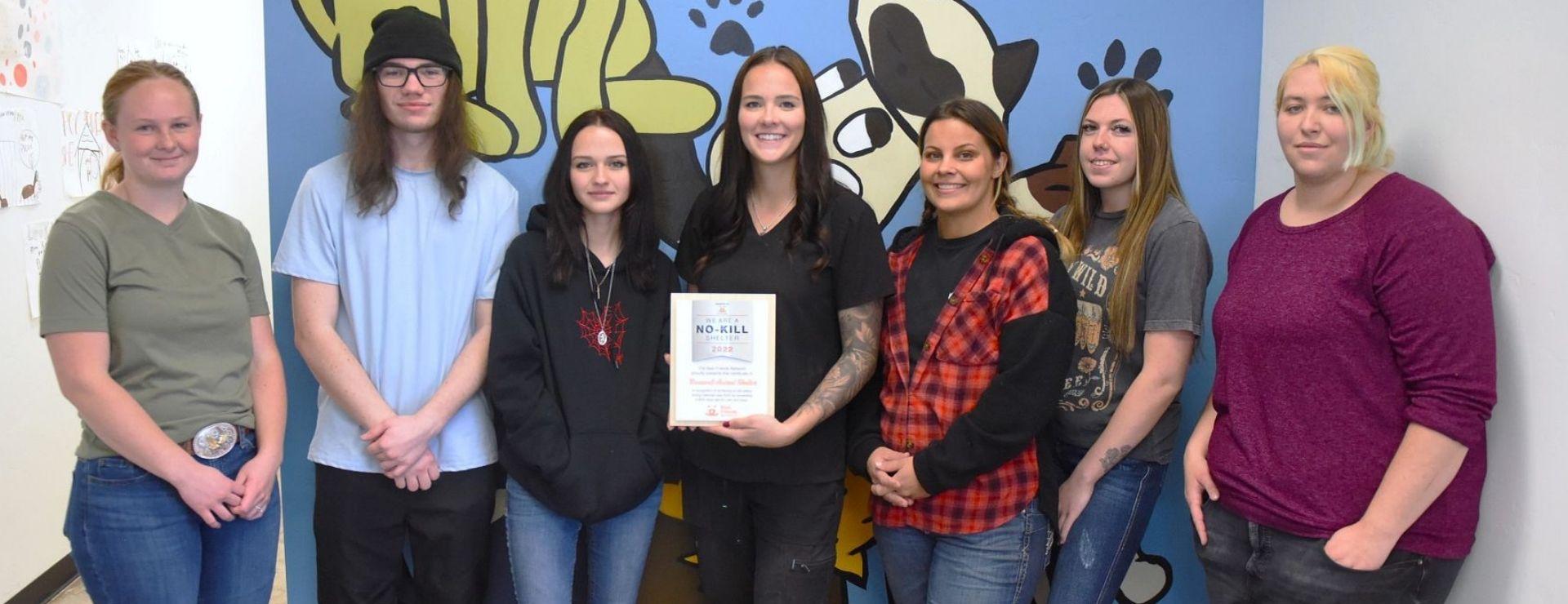 Group of previous plaque award recipients, posing in front of a mural