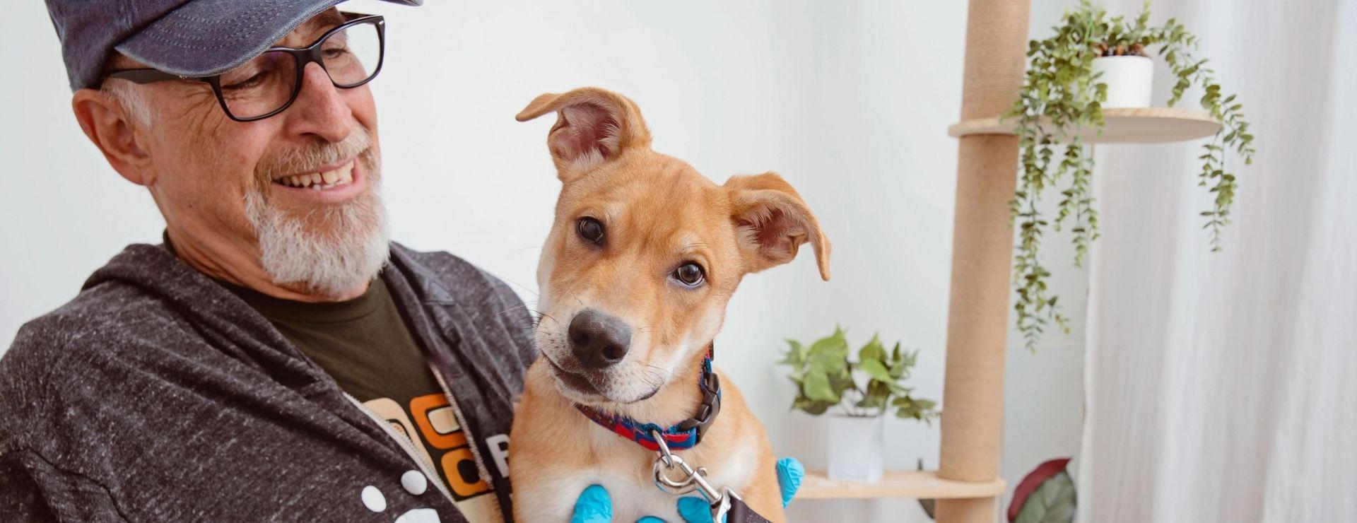 Image of an older man with a Best Friends sweatshirt holding a golden tan dog looking at the camera