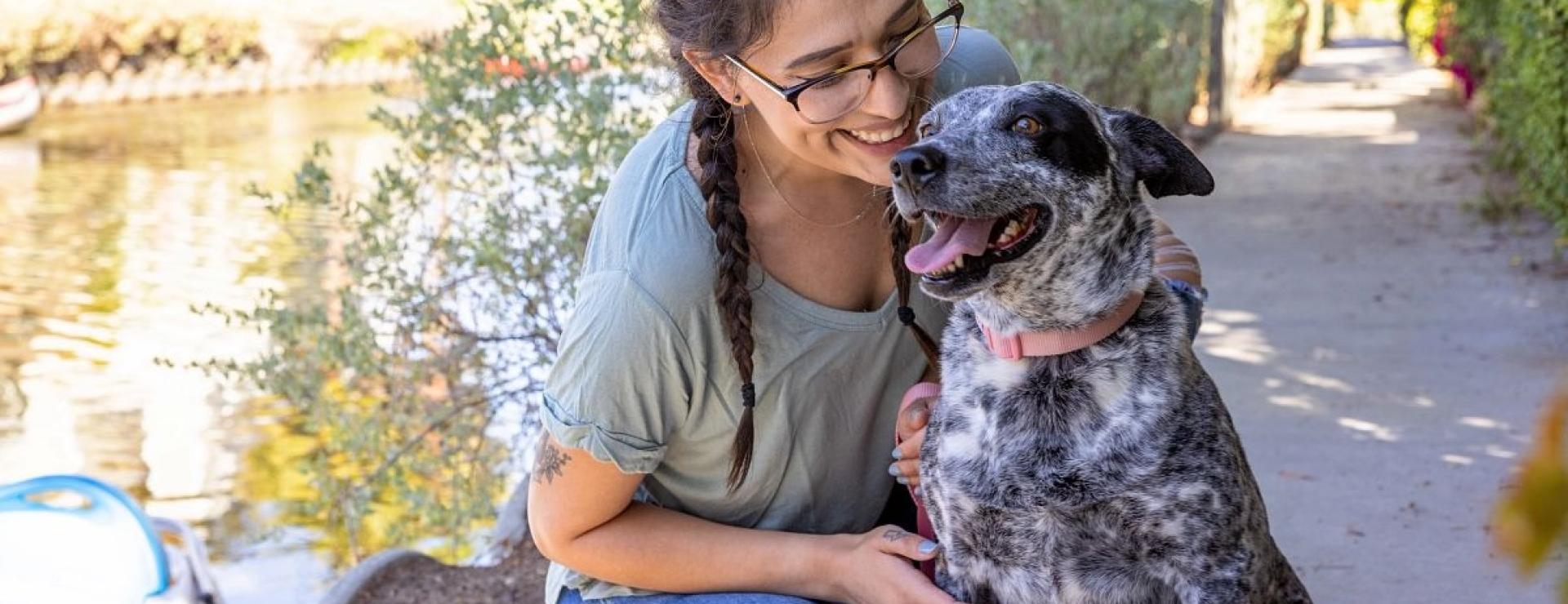 Young woman smiling warmly at her dog along a sunny canal.