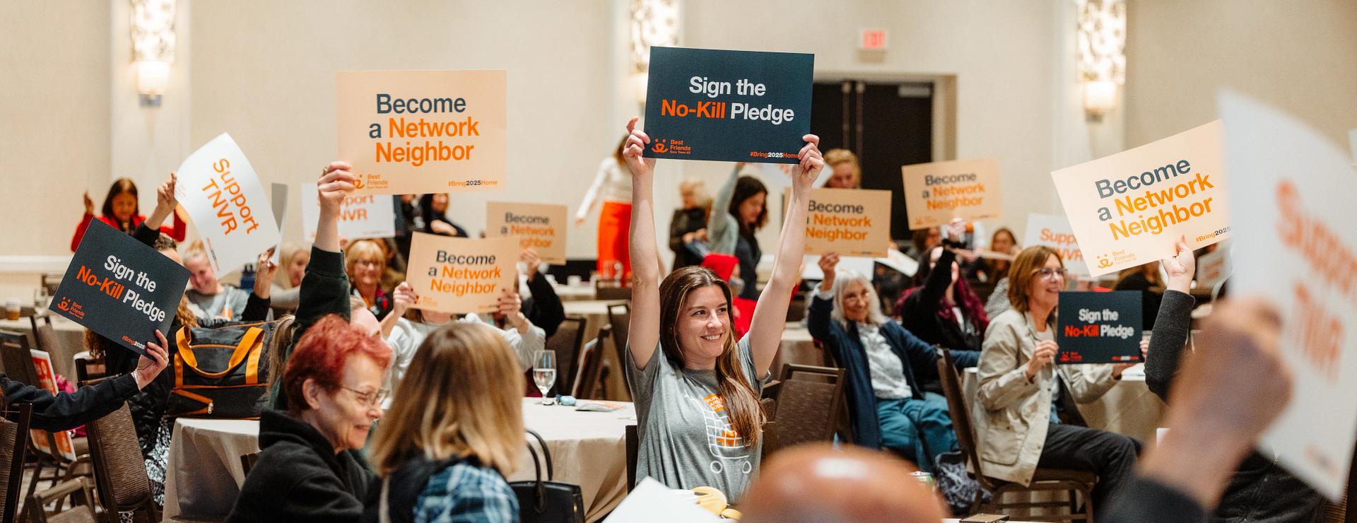 Attendees of the Chicago Bring No-Kill Home Summit smiling and holding up signs that say "Support TNVR", "Become a Network Neighbor", etc.