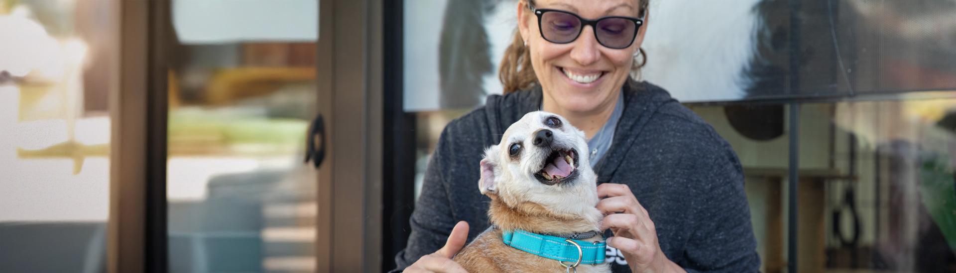Woman crouched with small dog outside of building 