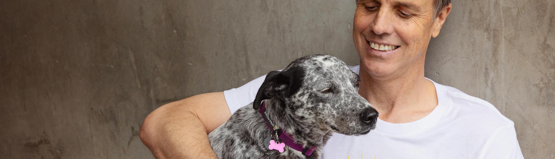 Smiling person sitting outside against a cement wall with a dog