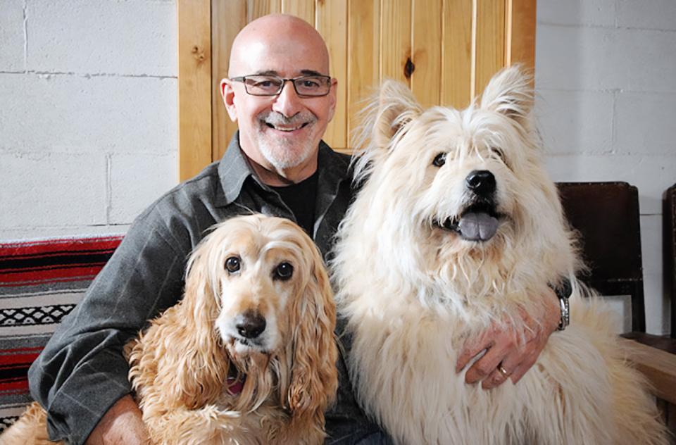 Francis Battista sitting with large brown and large white fluffy dogs
