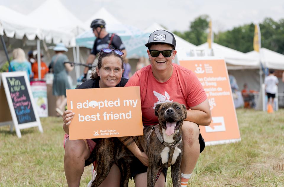 A couple with a dog holding an orange sign that says "I adopted my best friend"
