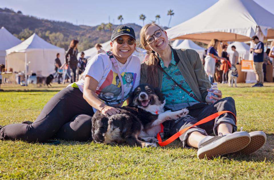 Two women sitting in the grass with a black and white dog on their laps