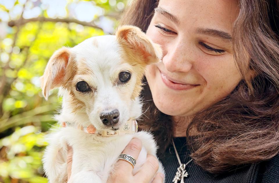 Woman holding small tan dog outdoors