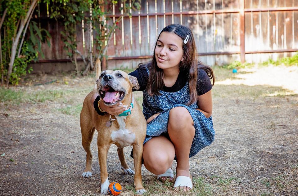 young woman squatting next to medium tan dog in yard