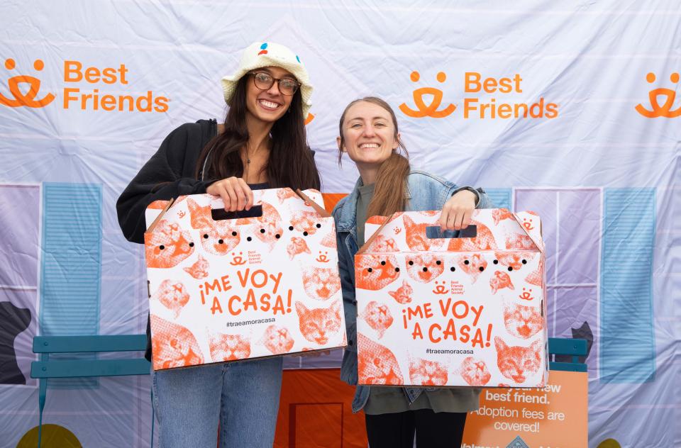 Two smiling people holding cats in Best Friends branded cardboard carriers