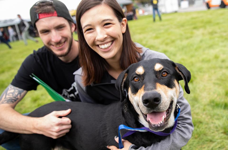 Couple hugging a smiling dog outside at a super adoption event