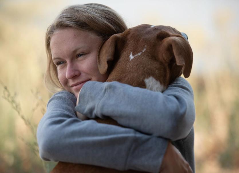 Woman hugging dog in a field.