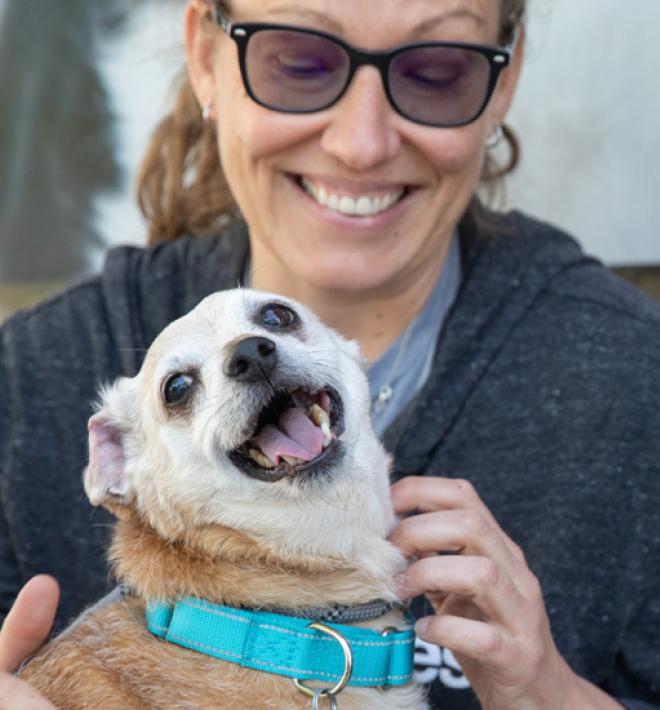 Woman crouched with small dog outside of building 
