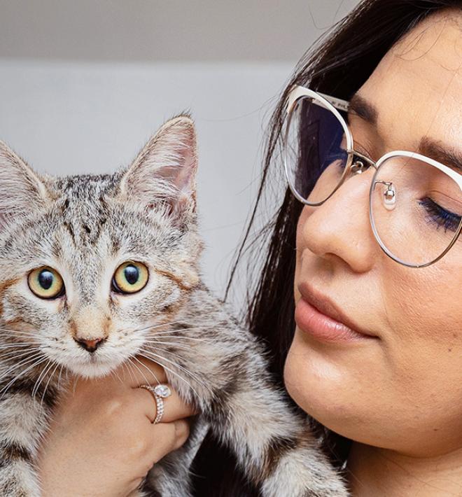 Person wearing glasses holding a tabby kitten