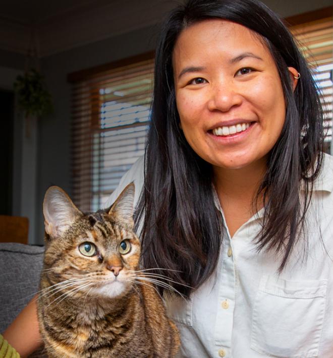Smiling person sitting on a couch with a cat next to them