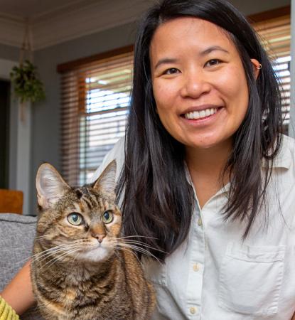 Smiling person sitting on a couch with a cat next to them